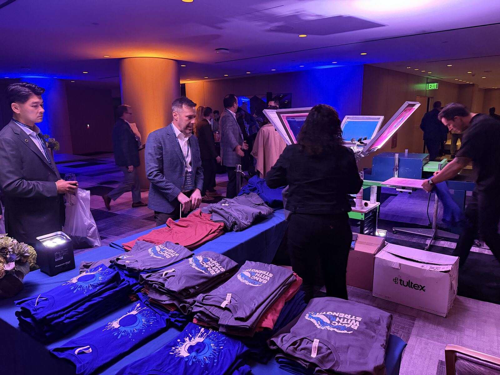 Professionally lit booth display showing screen-printed t-shirts with branded graphics at an event